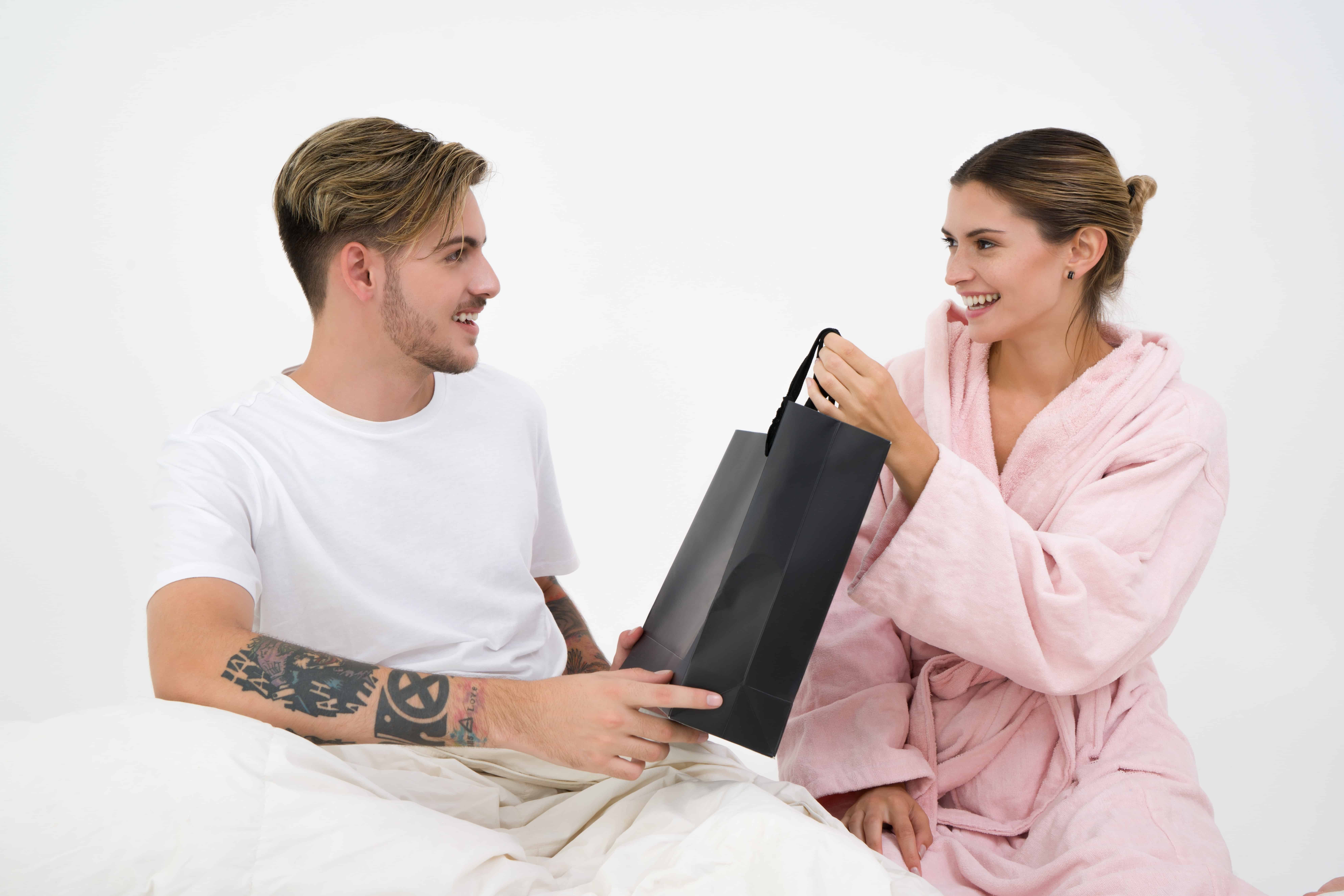 man and woman holding black bag while sitting on bed
