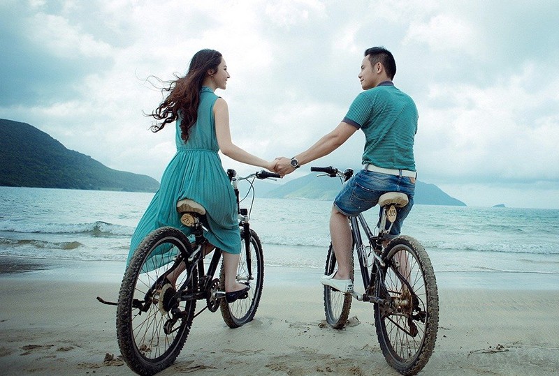 man and woman holding hands on the seashore while sitting on bike