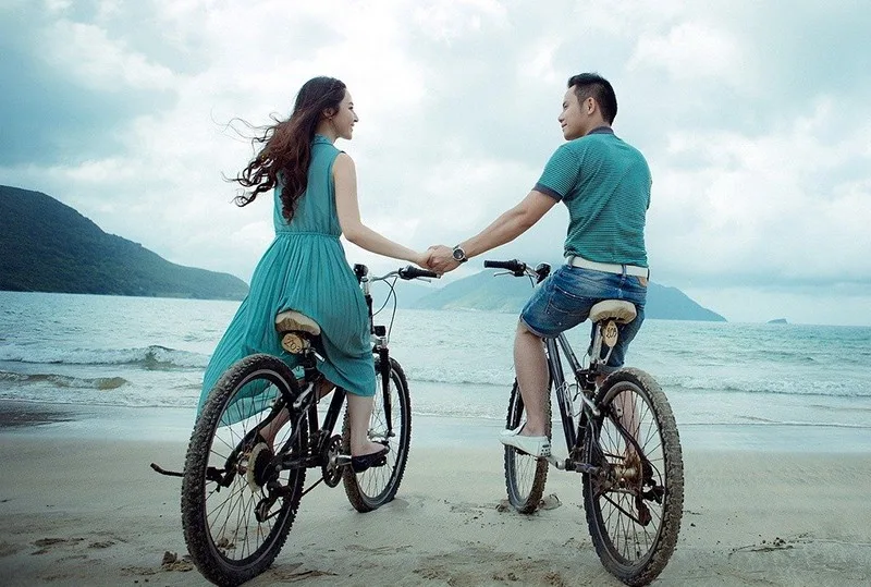 man and woman holding hands on the seashore while sitting on bike