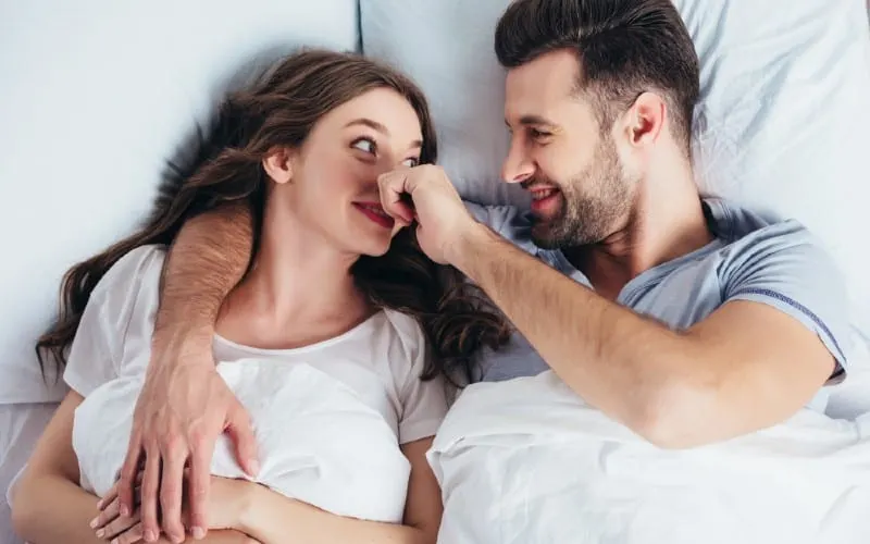 Happy woman in bed with man touching her nose