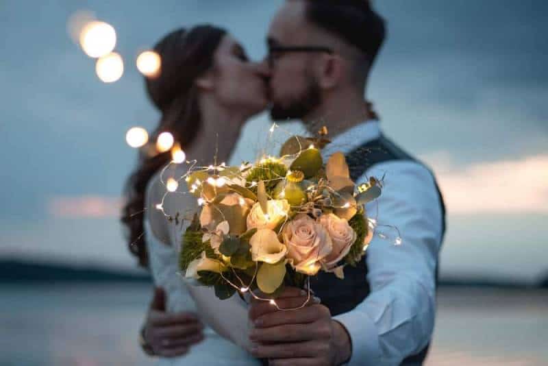 man and woman kissing holding white flowers