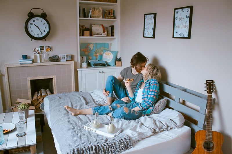 man and woman kissing on the bed while eating pizza