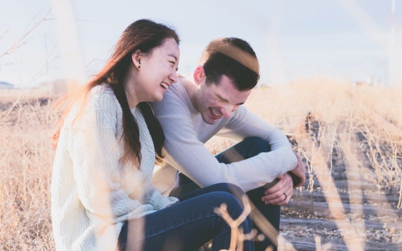 Laughing man and woman sitting on a field during daytime