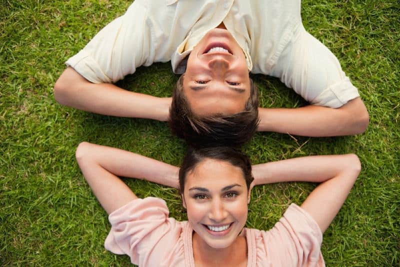 Jovem e mulher felizes deitados na relva, frente a frente, durante o dia