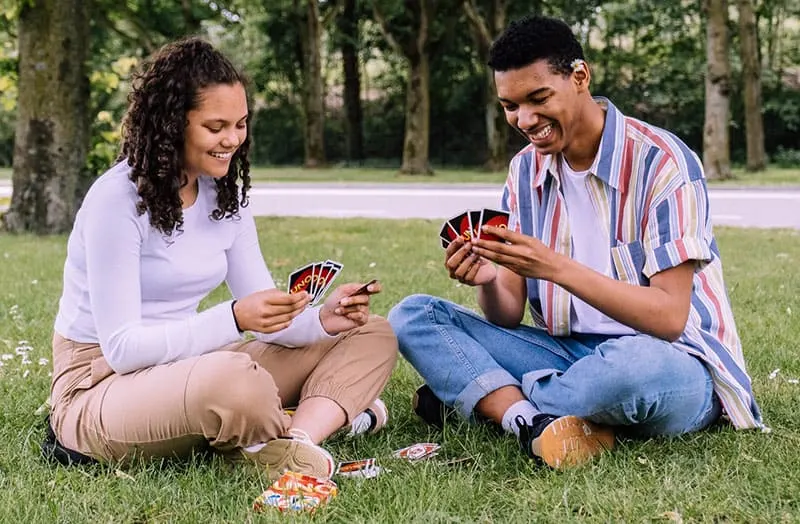 man and woman playing cards sitting in the green grass