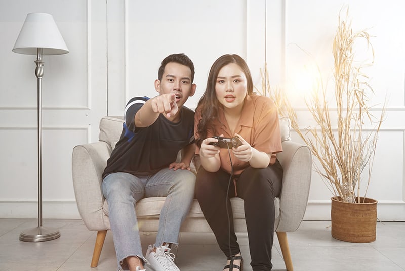 uomo e donna seduti su una poltrona mentre giocano ai videogiochi