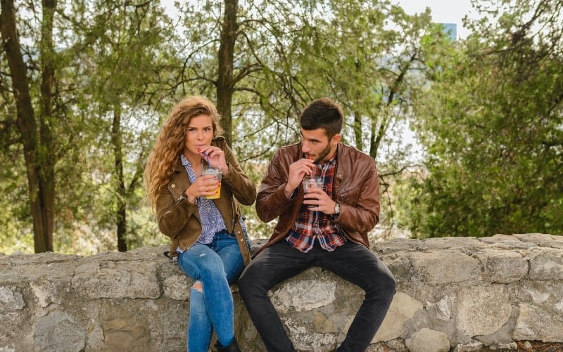 Hombre y mujer sentados y bebiendo zumo en la naturaleza durante el día