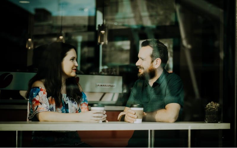 Uomo e donna si guardano in faccia mentre sono seduti a un tavolo con tazze di caffè