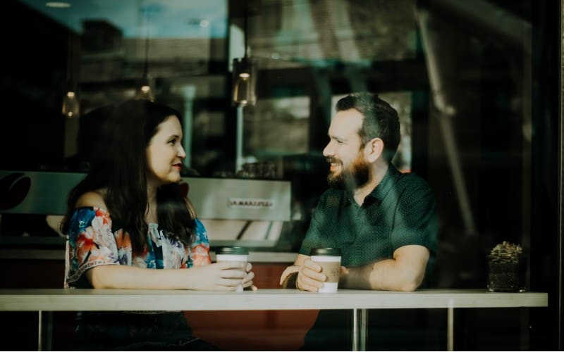 Man and woman faceing each other while sitting at a table with coffee cups on it