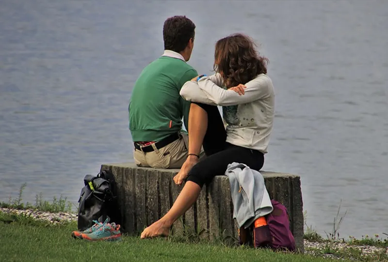 man and woman sitting beside the body of water during daytime