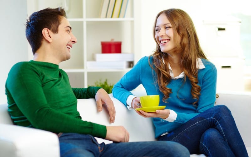 Homem e mulher sorridentes sentados num sofá enquanto conversam