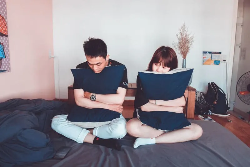 man and woman sitting on bed both embracing blue pillows