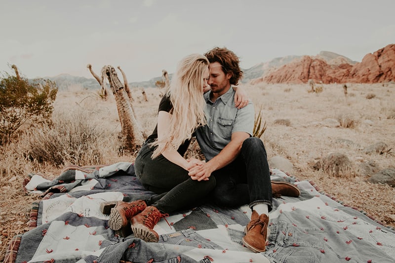 man and woman sitting on blanket in the nature