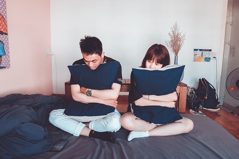 hombre y mujer sentados en la cama abrazados almohada