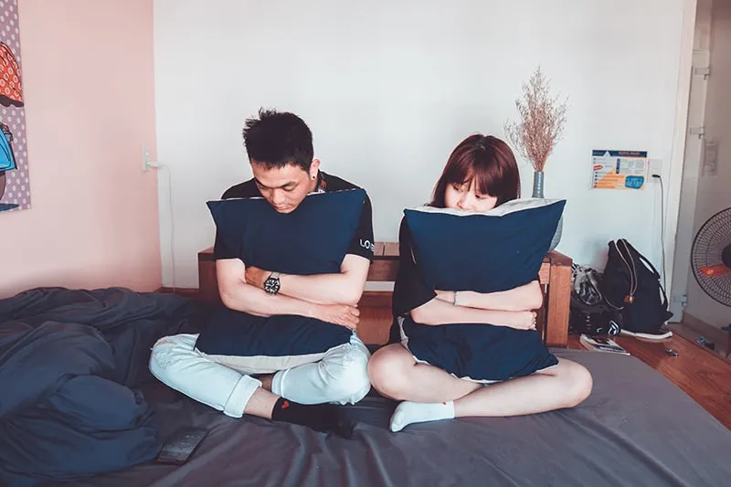 man and woman sitting on the bed while hugging pillow