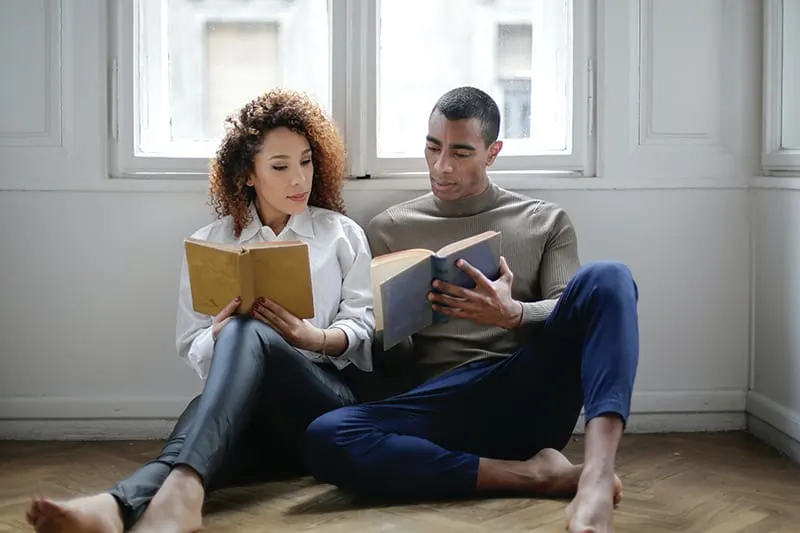 man and woman sitting on the floor reading the book