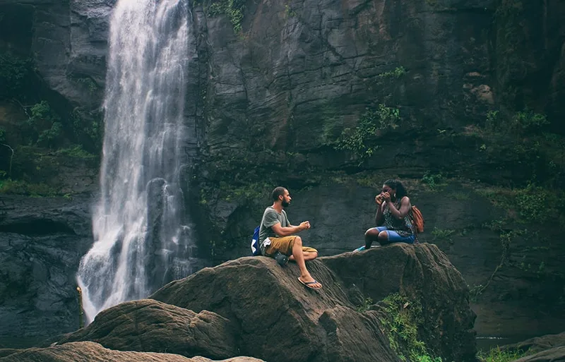 man and woman sitting on the rock near the waterfall