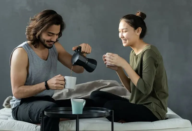 man and woman sitting on bed man pours coffee