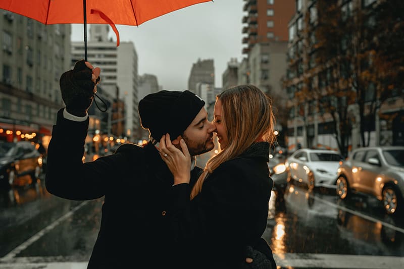 homem e mulher de pé sob um guarda-chuva na estrada