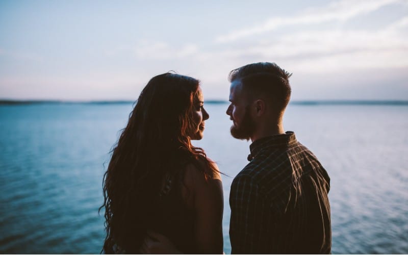 man and woman standing while looking at each other near body of water
