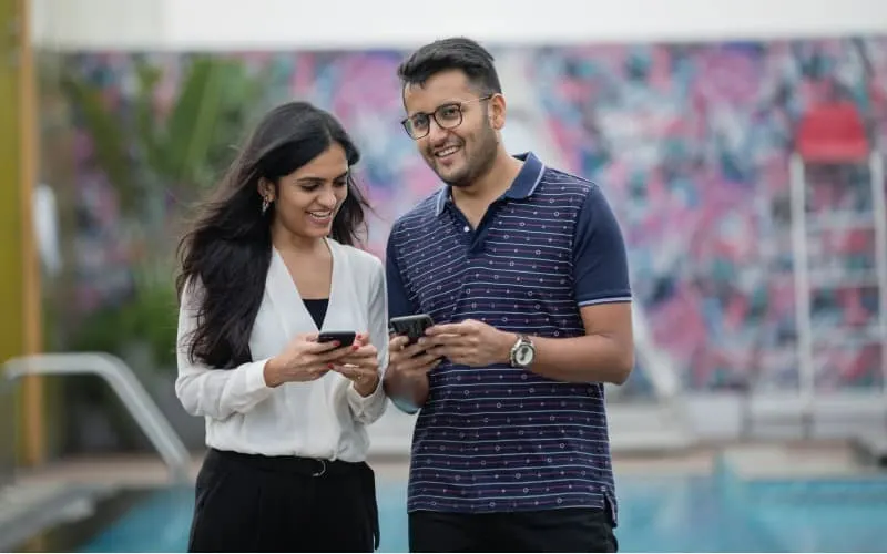 man and woman standing n the street with phones in their hands smiling