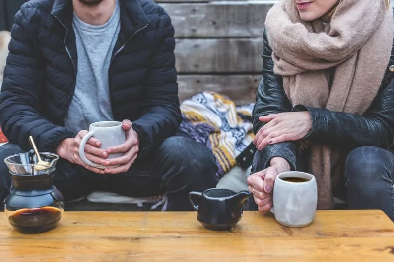man and woman talking holding coffee in winter clothes