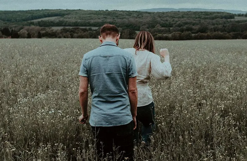 man and woman walking in the middle of the fields
