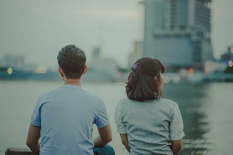 man and woman watching body of water and concrete buildings