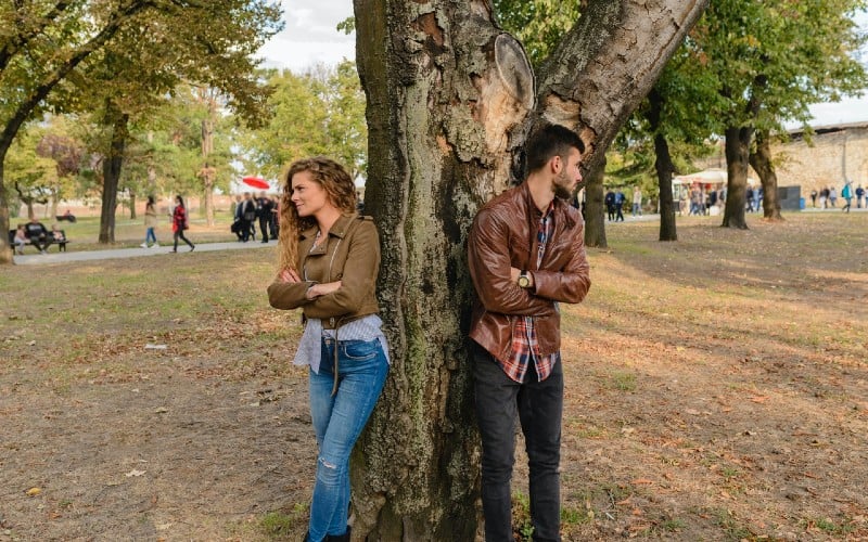 Man and woman wearing leather jackets standing under tree in a park