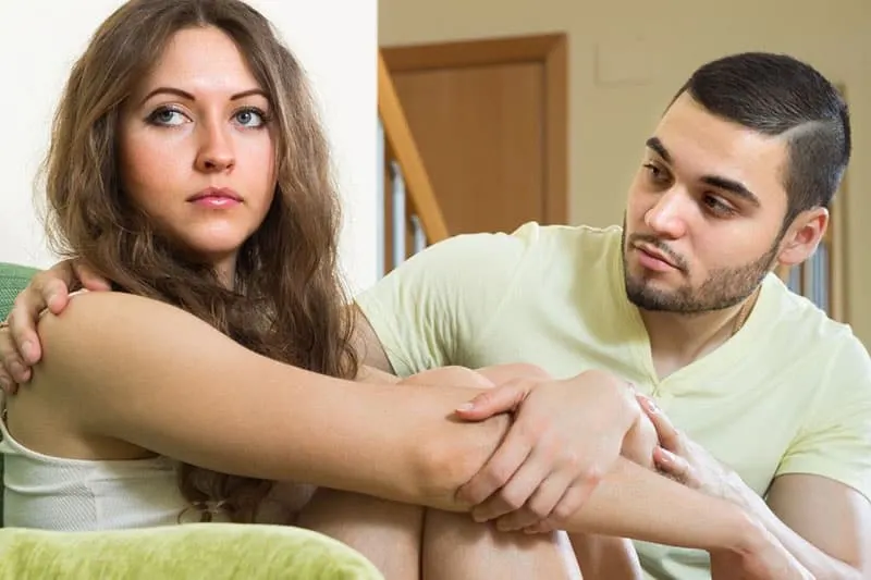 man asking forgiveness to an upset woman with knees tucked