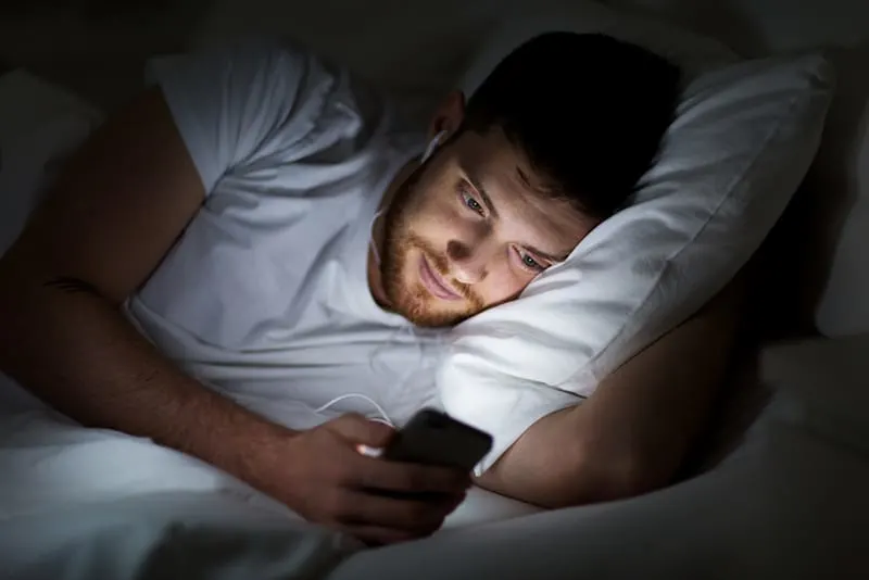 Man in bed with earphones on and using smartphone