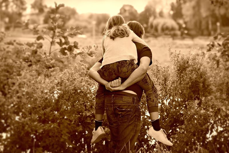 man caring a child on his back in deep grass