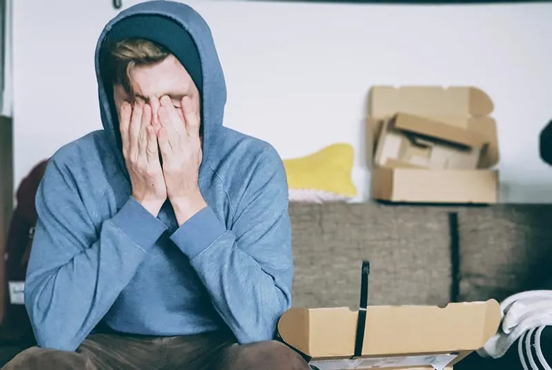 man covering face with both hands while sitting on the sofa