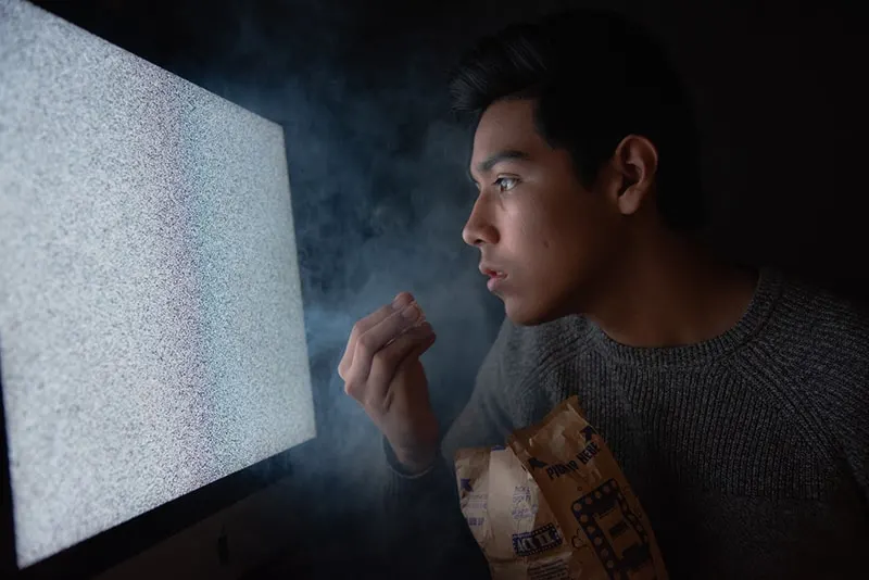 man eating popcorn while staring at tv