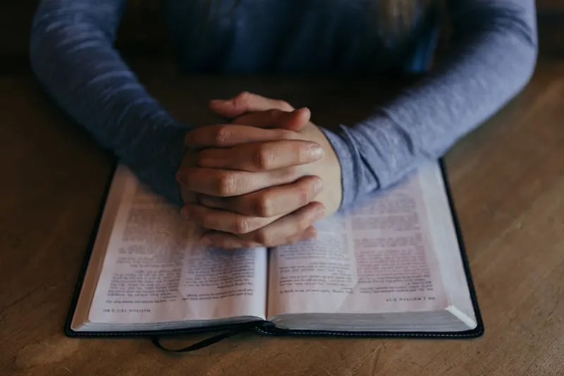 man folding his hands on the book