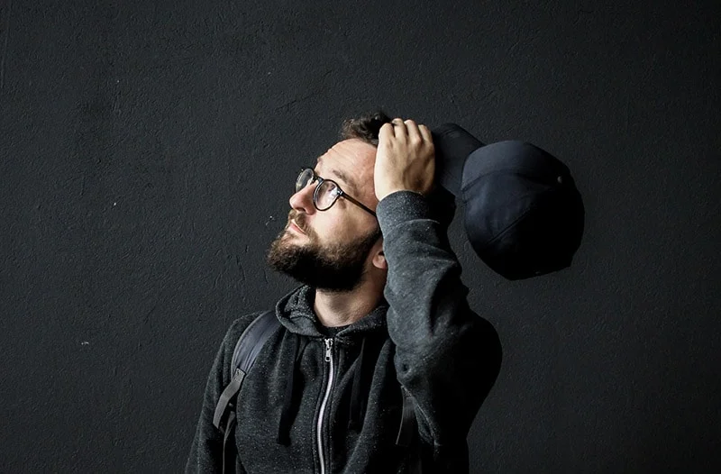 Man wearing hoodie and eyeglasses holding cap
