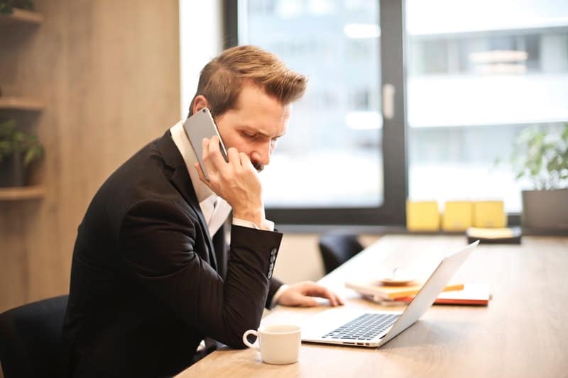 man having phonecall while looking at a laptop in front of him