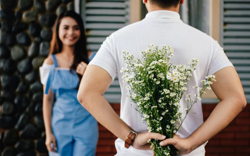 Man holding flowers at his back in front of woman