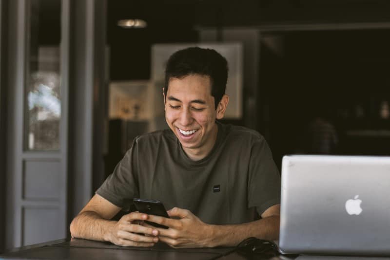 hombre sonriente usando el teléfono junto a un MacBook plateado