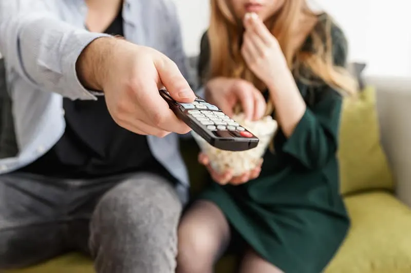 man holding remote control beside woman eating popcorn