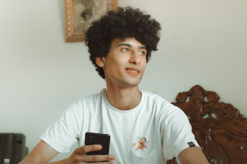 homem de t-shirt branca segurando um smartphone preto no interior