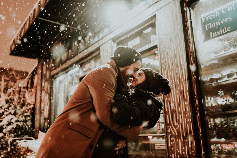 man holding woman while is snowing