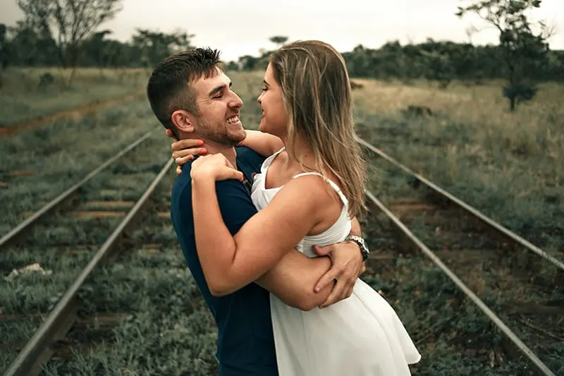 man holding woman while standing on rail track