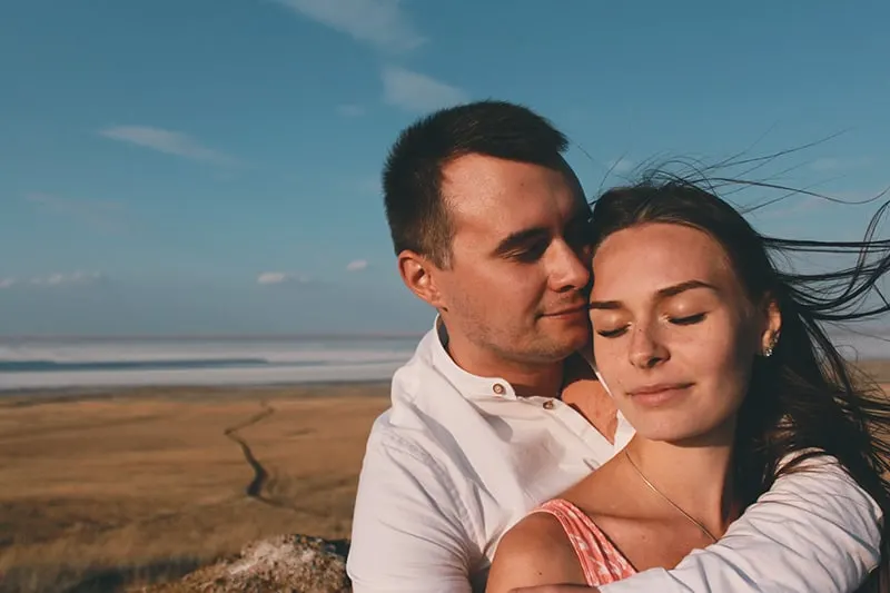 man hugging woman from the back on the seashore