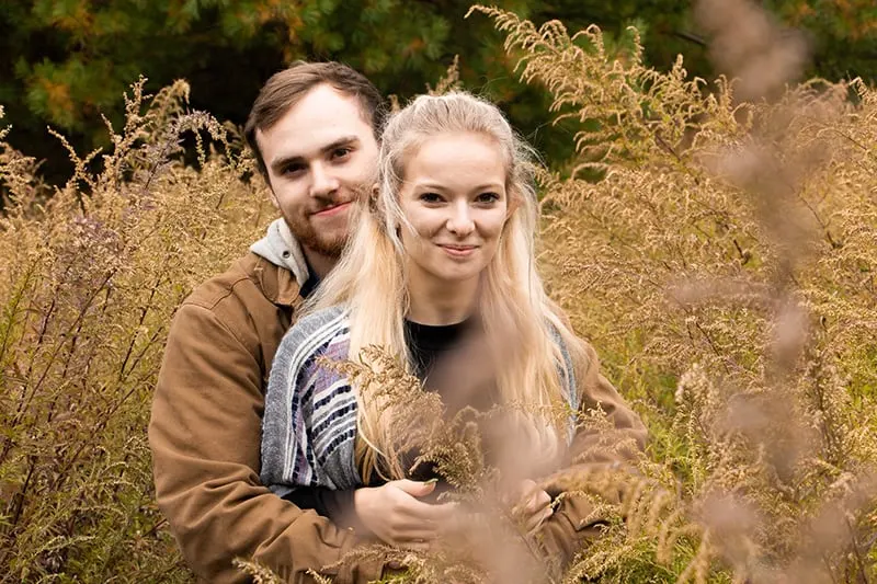 man hugging woman with long blonde hair while sitting in the field