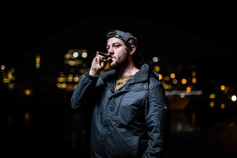 man in black jacket standing while smoking cigar