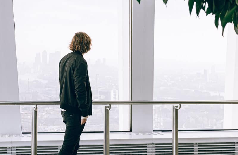 man in black jacket looking outside thru the big glass windows