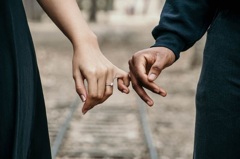 hombre en negro de manga larga sosteniendo la mano de una mujer con un anillo
