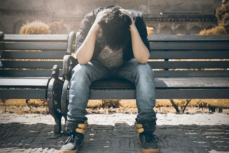 man in black shirt sitting on bench with two hands on his head