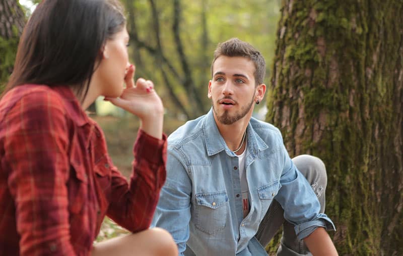 man in blue shirt talking to a girl in red top near a tree